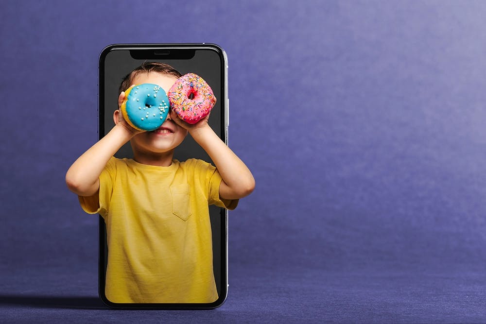 smiling boy inside smart phone looking out with donuts for binoculars